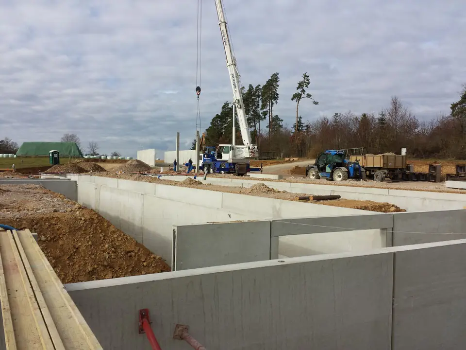Rohbau eines Kellergeschosses aus Betonfertigteilen, daneben ein Autokran